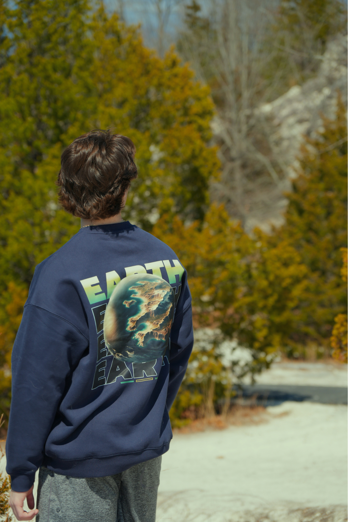 Person wearing a navy sweatshirt with 'Earth' design outdoors in nature traveling